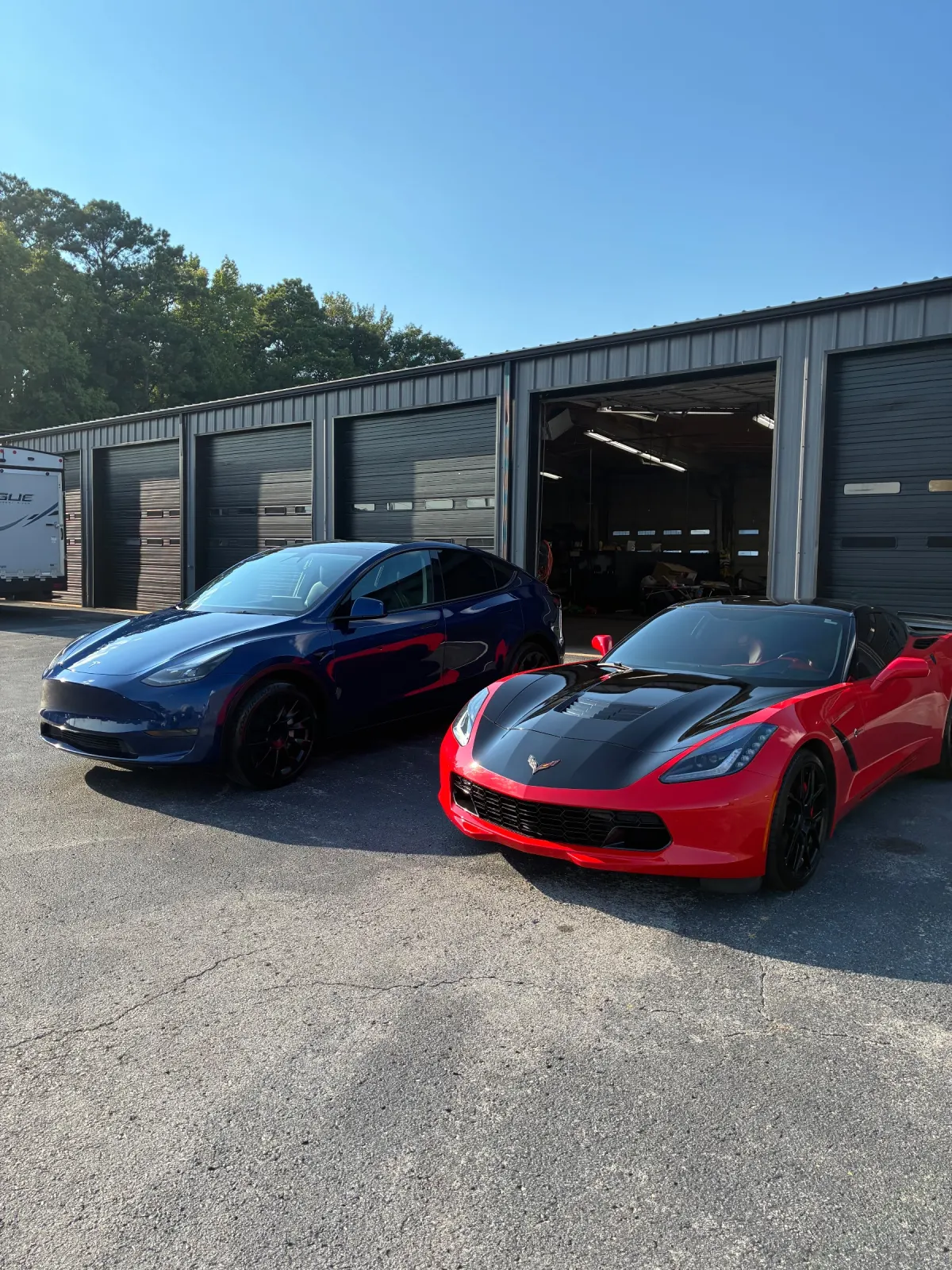 Blue Tesla Model Y and red Corvette Stingray detailed side by side outside the shop bays